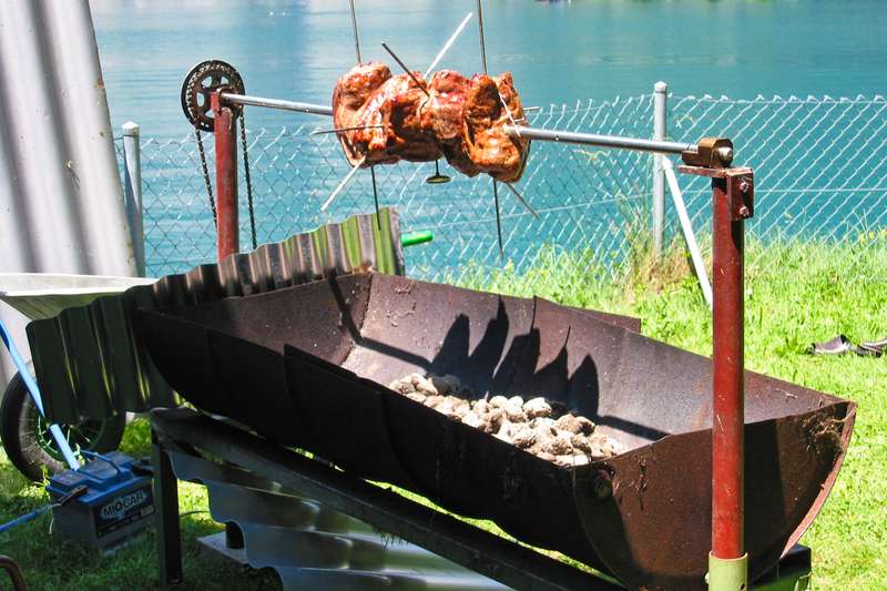 Saftiger Spießbraten auf einem rustikalen, selbstgebauten Drehspieß-Grill am Seeufer.