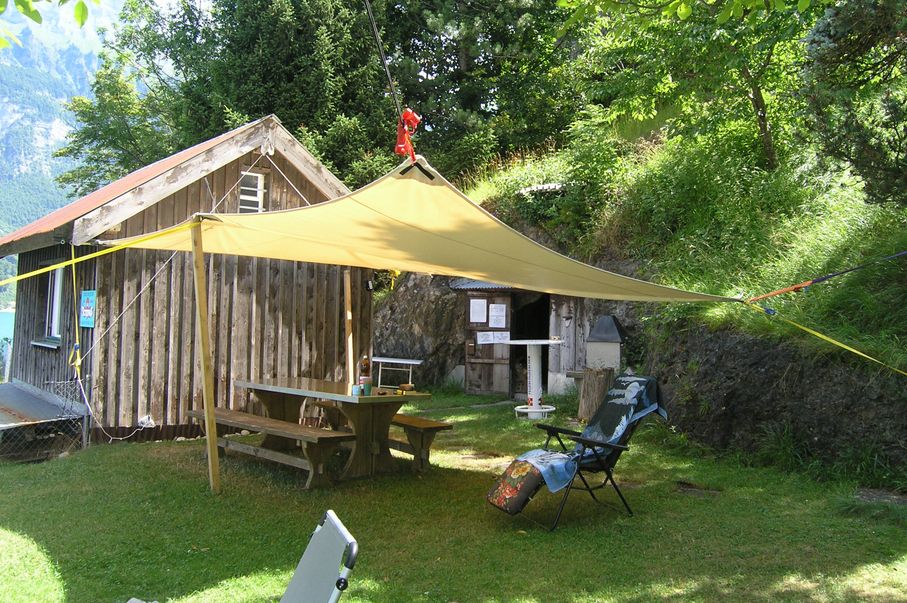 Clubhaus mit Dreieckblache, darunter ein Tisch mit Bank und Liegest&uuml;hle