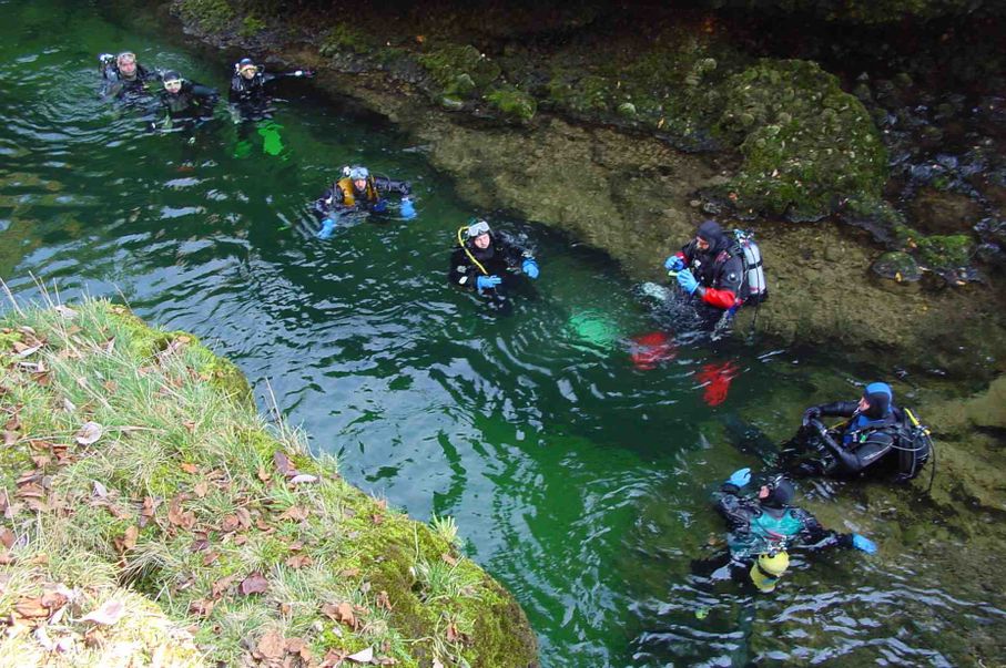 Taucher steht am Rand eines tiefgr&uuml;n schimmernden Flussbetts vor dem abtauchen.